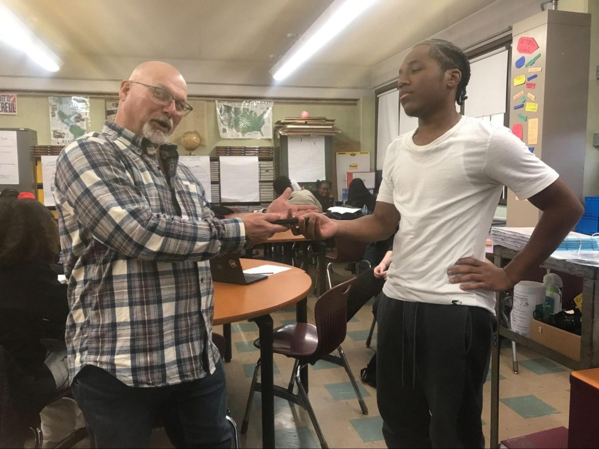 Mr. Thompson takes Junior Jaylyn Hardy's phone as he looks moody. In 208 which is Mr. Thompson's classroom.